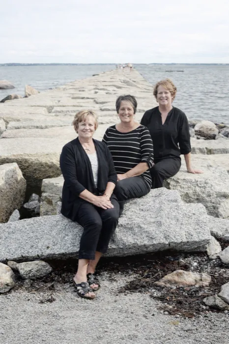The owners of Just Friends Hair Design standing together on the rocks along the Rockland, Maine breakwater